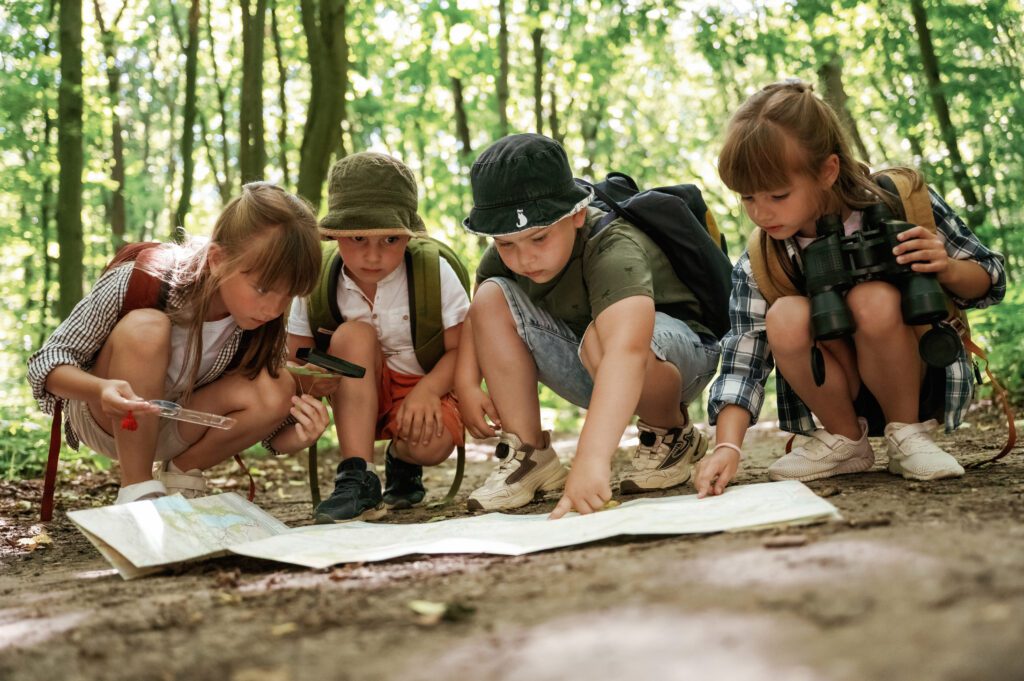 On the ground with map. Kids in forest at summer daytime together.