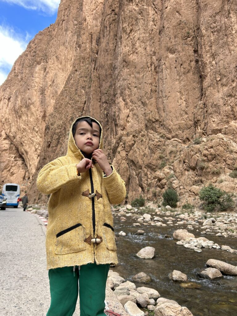 Child in a yellow coat beside the road and river in Todra Gorge, Morocco