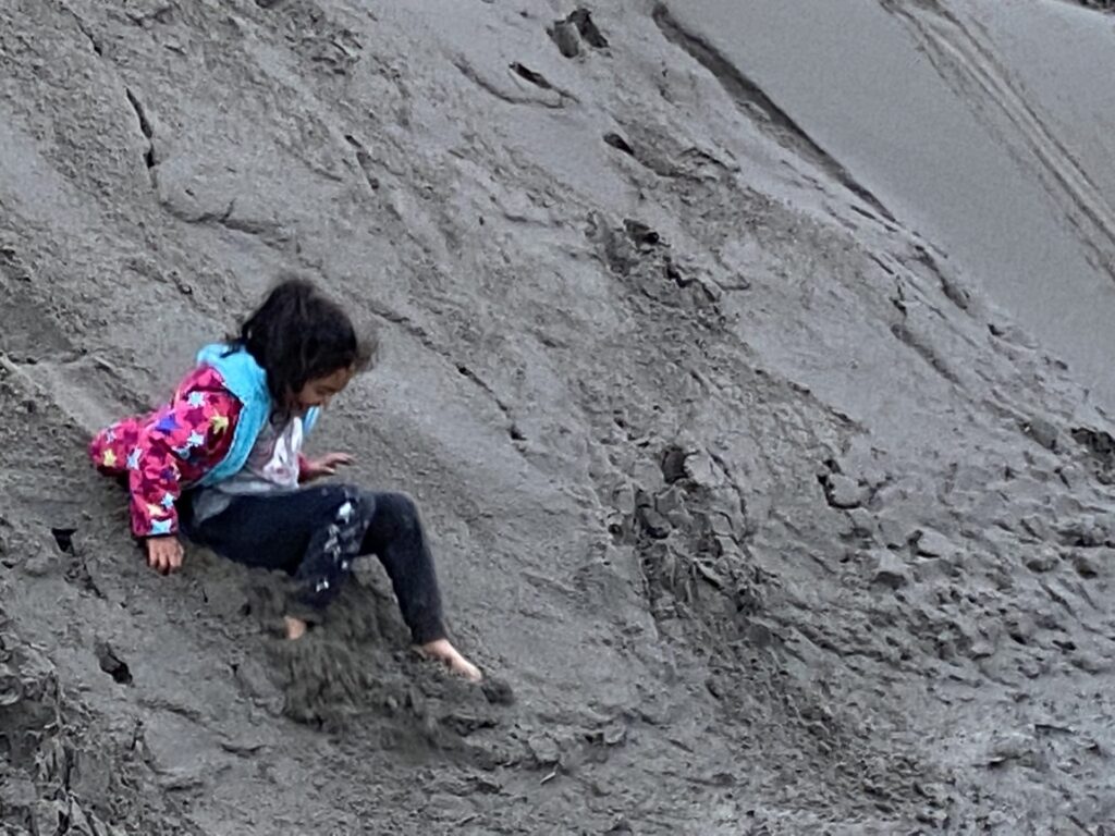 Child scrambling up a grey sand dune slope near Warrenton, Oregon