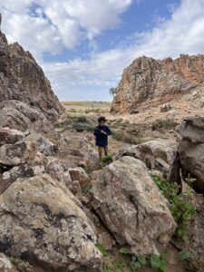 Child walking through boulders below rock walls at a family crag in Morocco