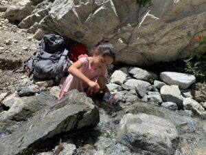 Child crouching by backpacks and rocks at the base of a rock wall
